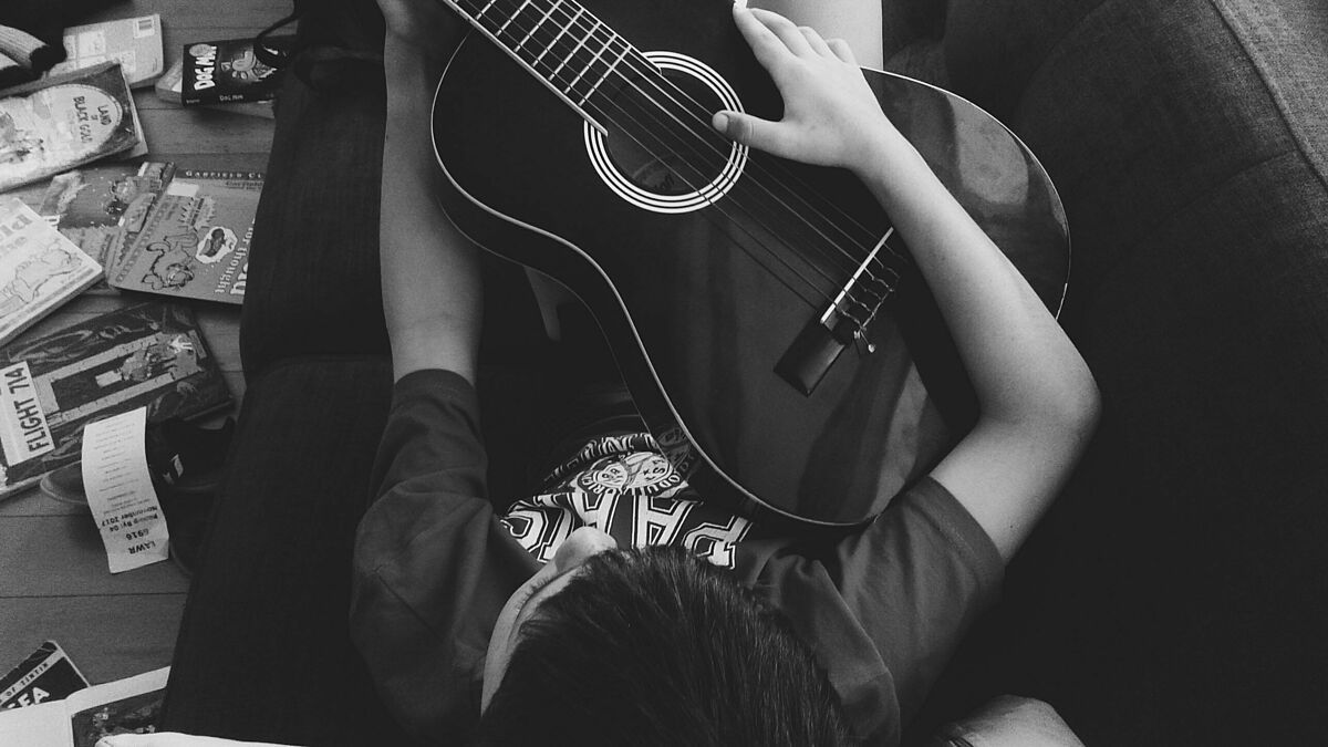 Man der auf Couch liegt und Gitarre spielt @pexels.com