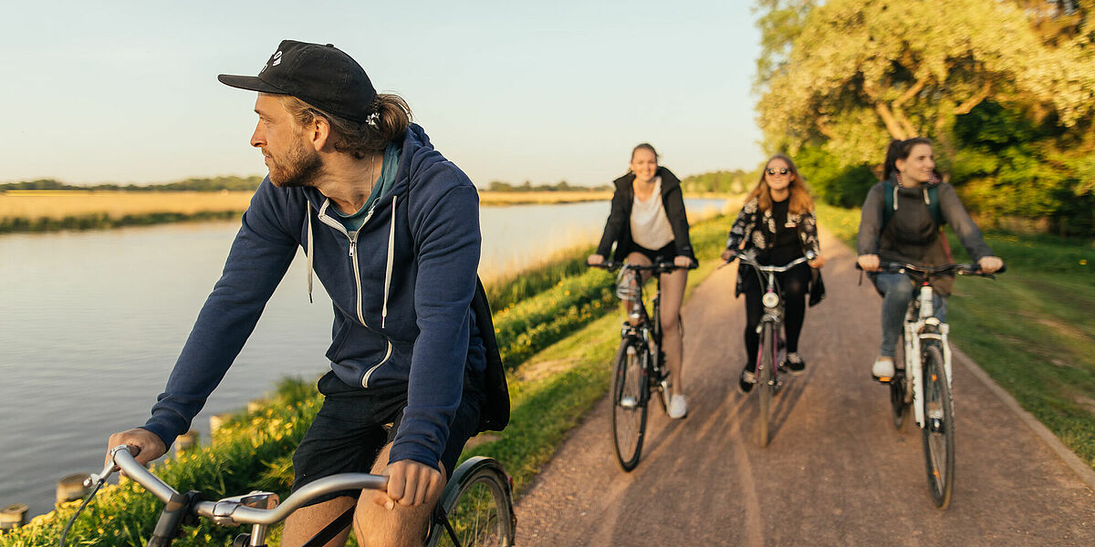 Eine Gruppe Radfahrer*innen auf dem Treidelpfad am Flüsschen Ryck.